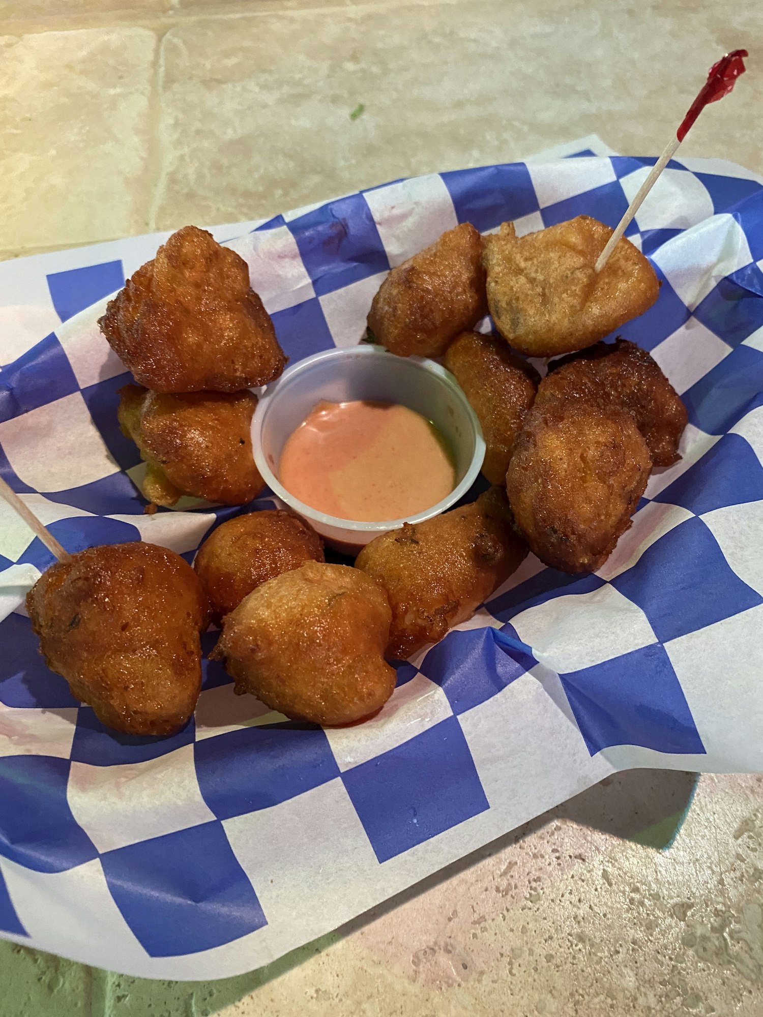 A bowl of conch fritters sitting on a blue and white paper lining